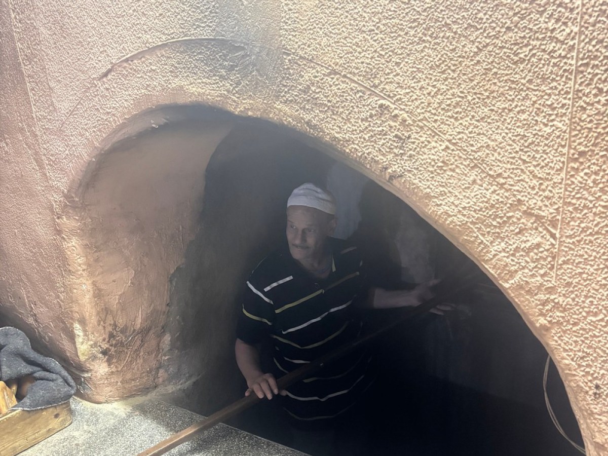 Man standing in front of a traditional stone oven with a wooden paddle in hand.
