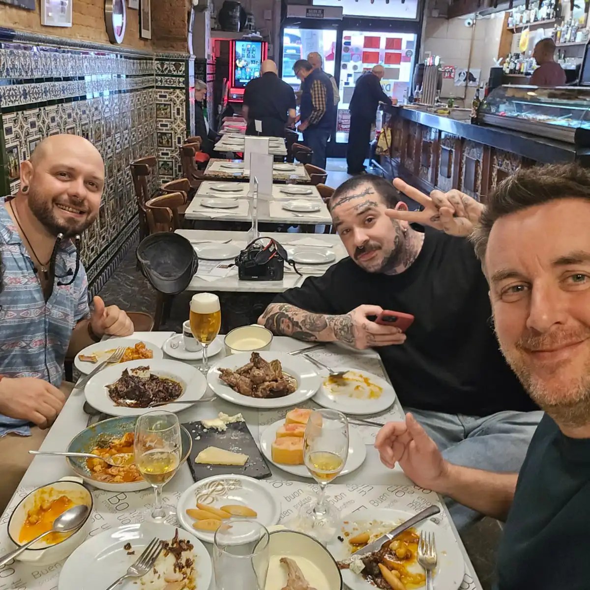Three men in a restaurant, smiling with plates of food and beverages on the table.