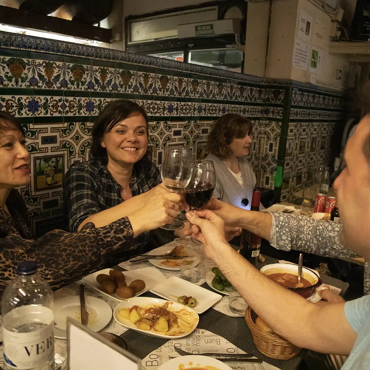 Group of people toasting with wine around a restaurant table, enjoying a meal.