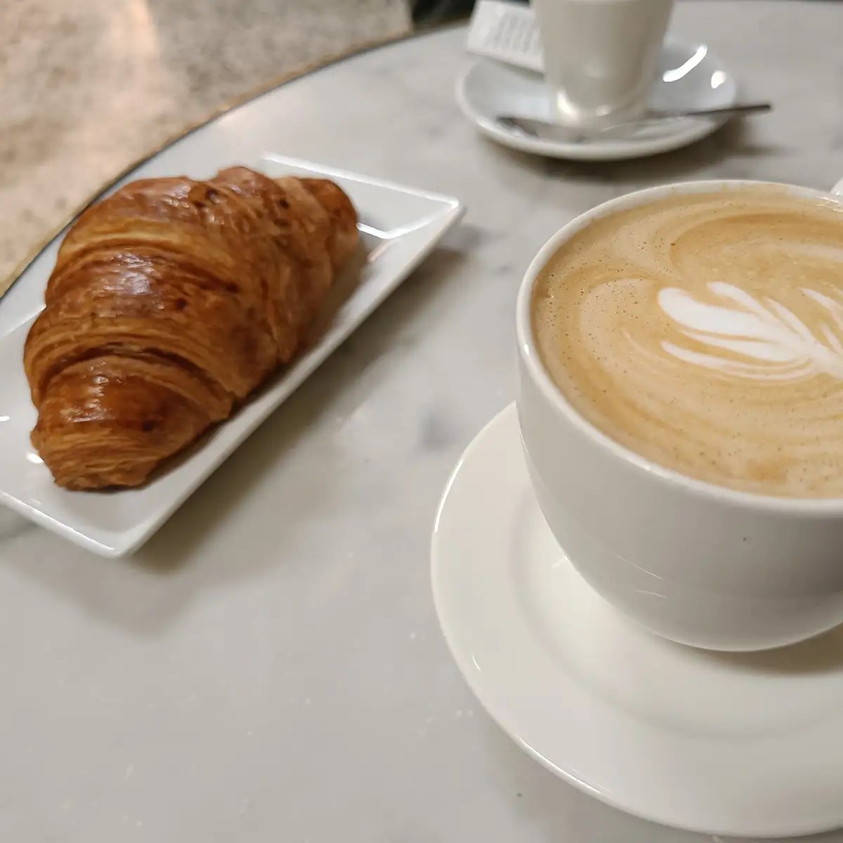 A latte with art and a croissant on a marble table.