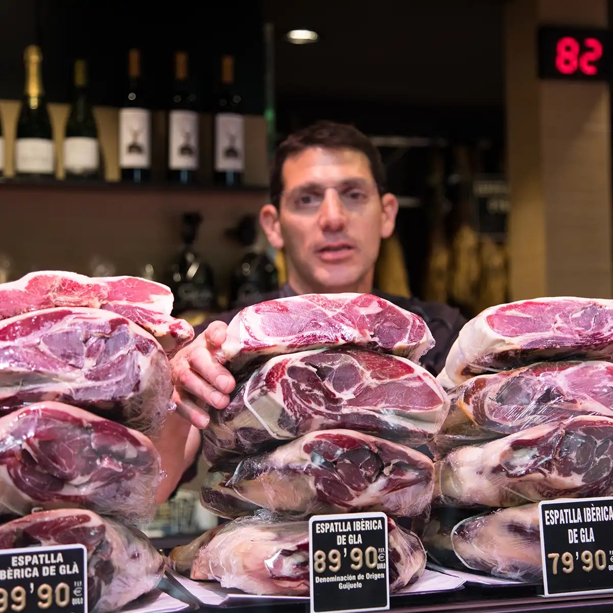Man arranging packaged Iberian ham on a counter with wine bottles in the background.