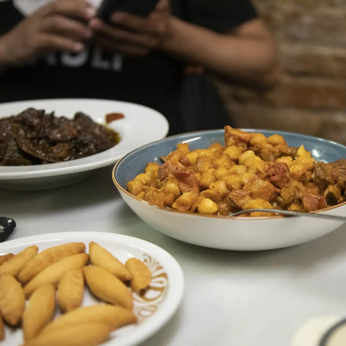 Three dishes: chickpea stew, dark meat dish, and small fried pastries on a table.