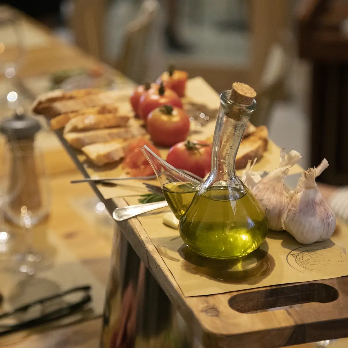 Olive oil decanter, garlic, tomatoes, and bread on a wooden board.