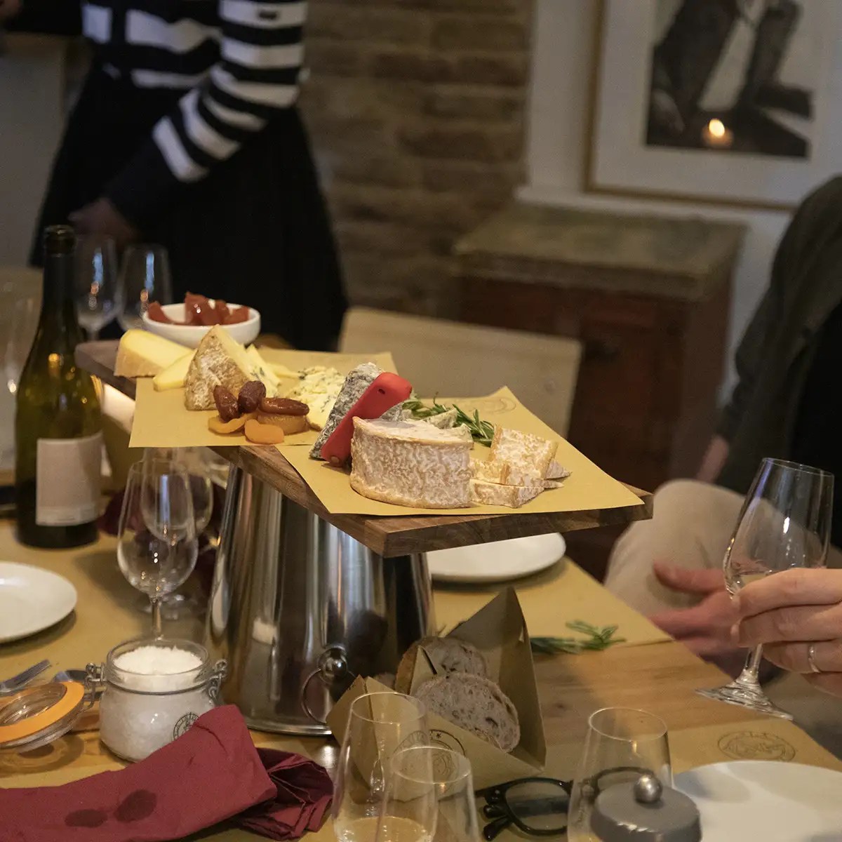 Cheese platter with various cheeses, fruits, and wine glasses on a wooden table.