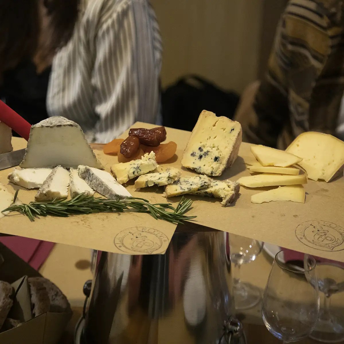 Cheese platter with various cheeses, dried fruits, and herbs on a table.