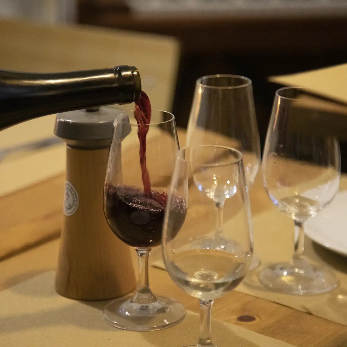 Red wine being poured into one of several empty glasses on a table.