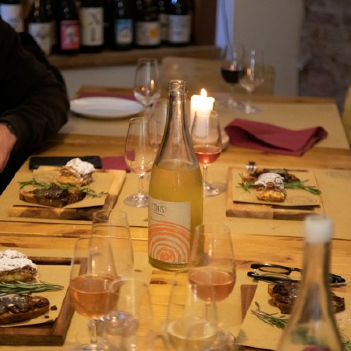 Dinner table with platters, wine, and glasses, surrounded by people.
