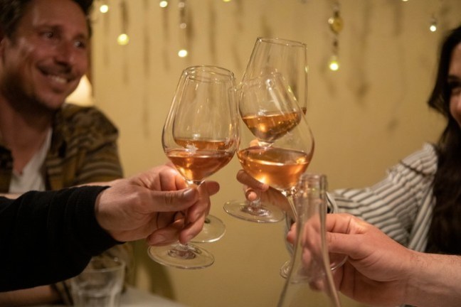 People toasting with rose wine glasses at a gathering.