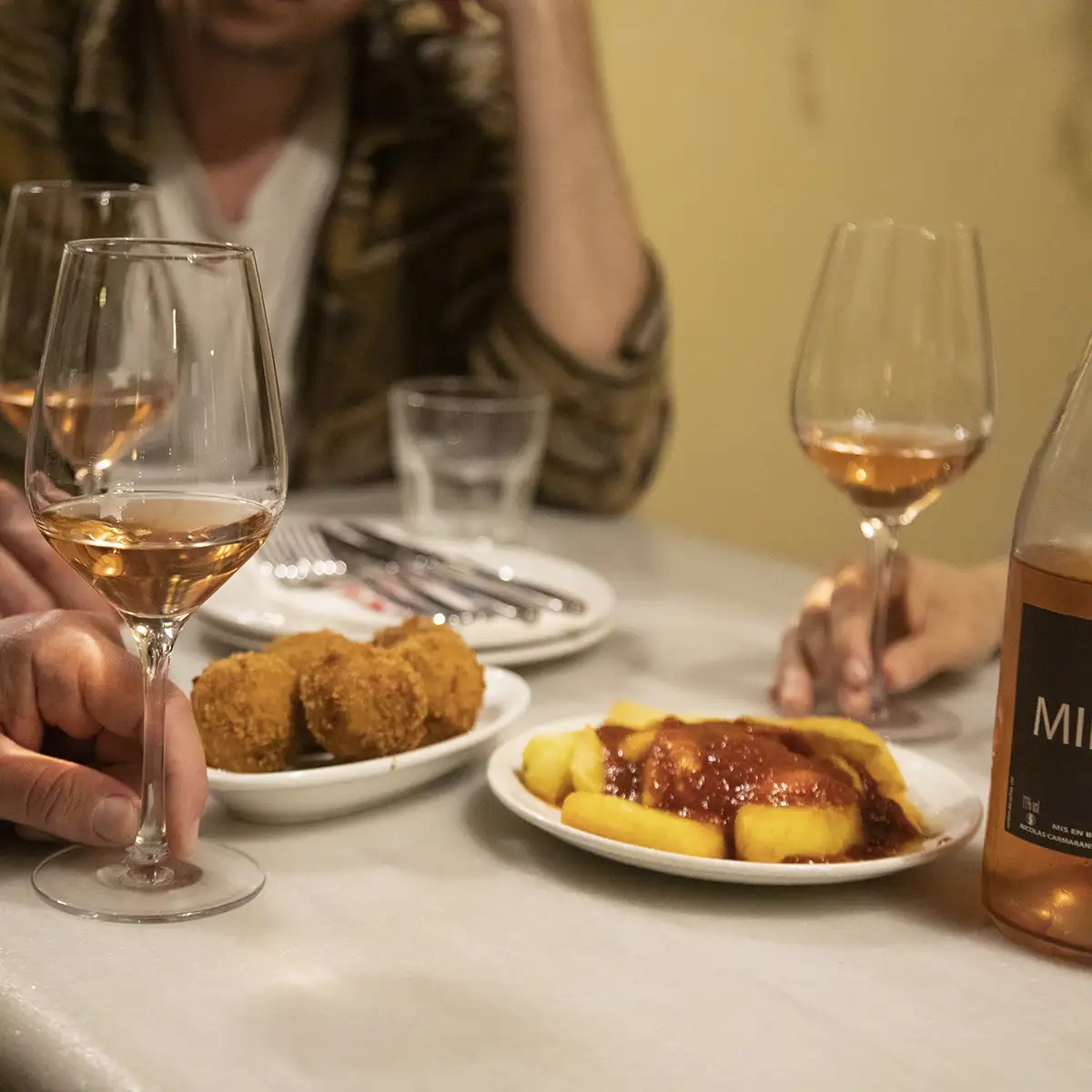 People sharing wine and snacks at a table with croquettes and fries.