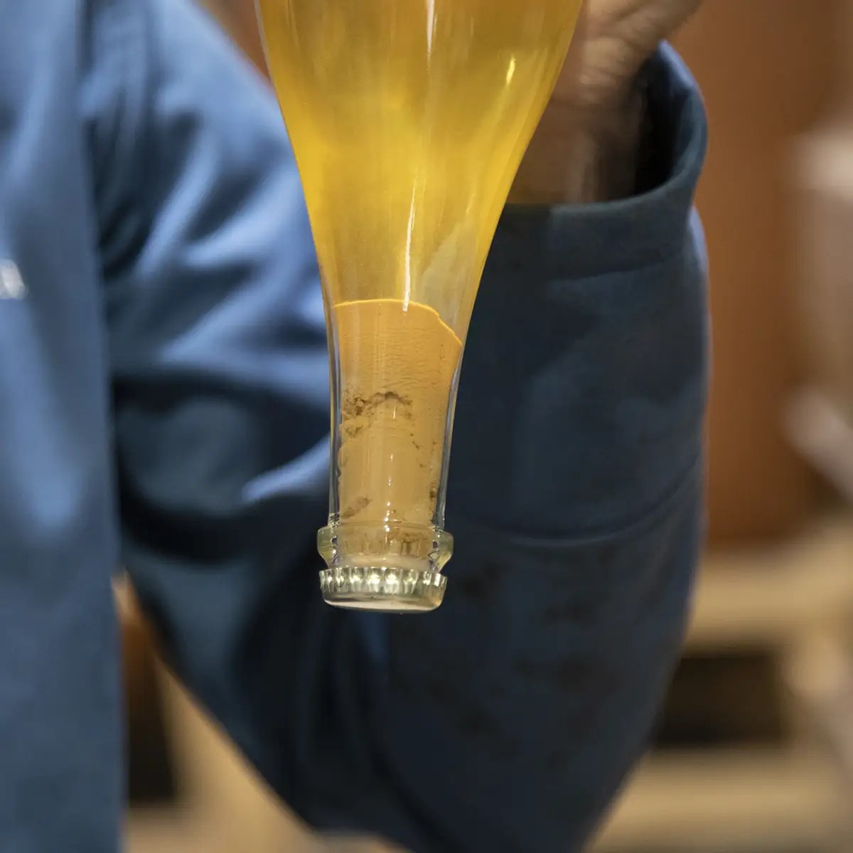 Person holding partially filled, inverted bottle of yellow liquid, showing sediment at the neck.