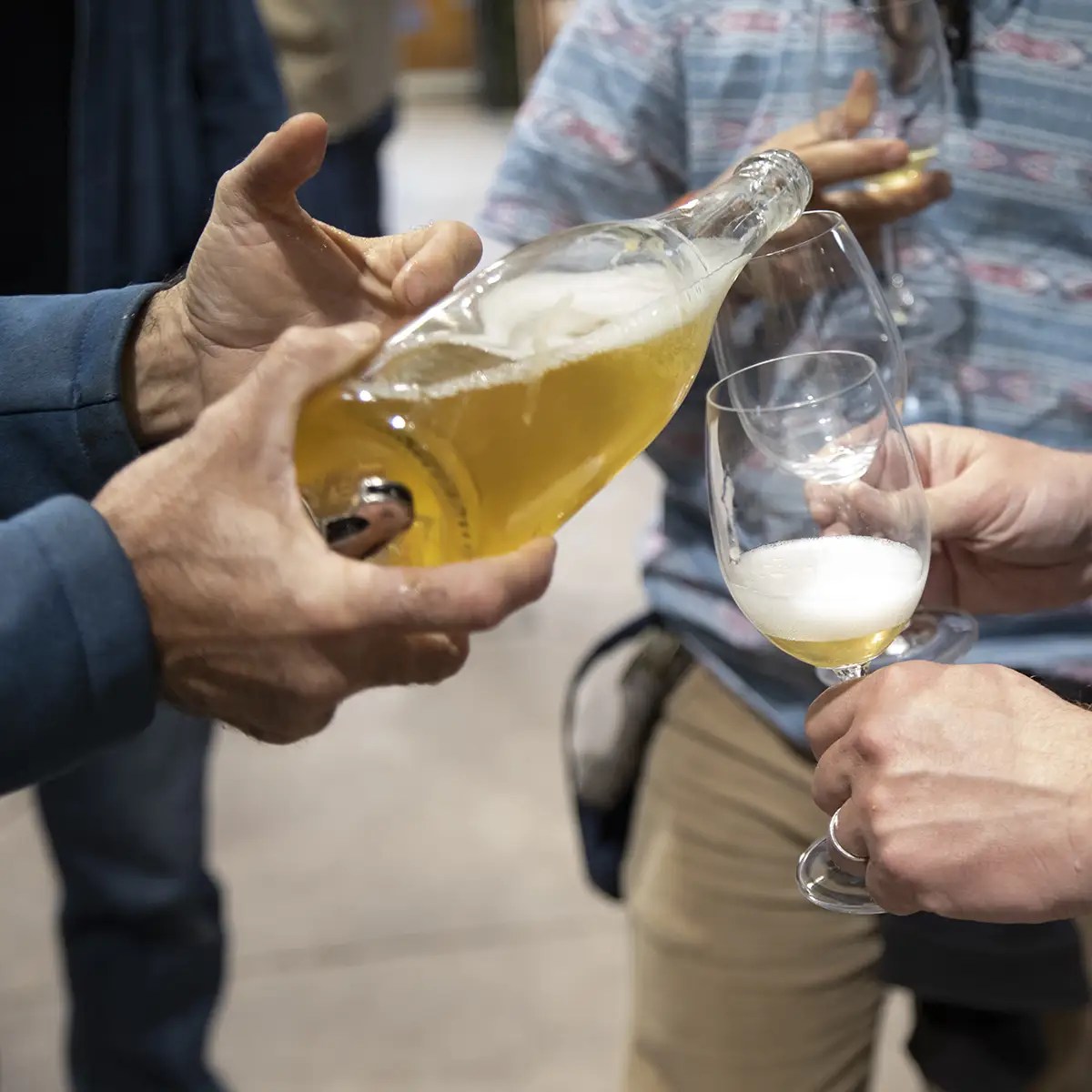 Person pouring beer from a bottle into a glass held by another person.