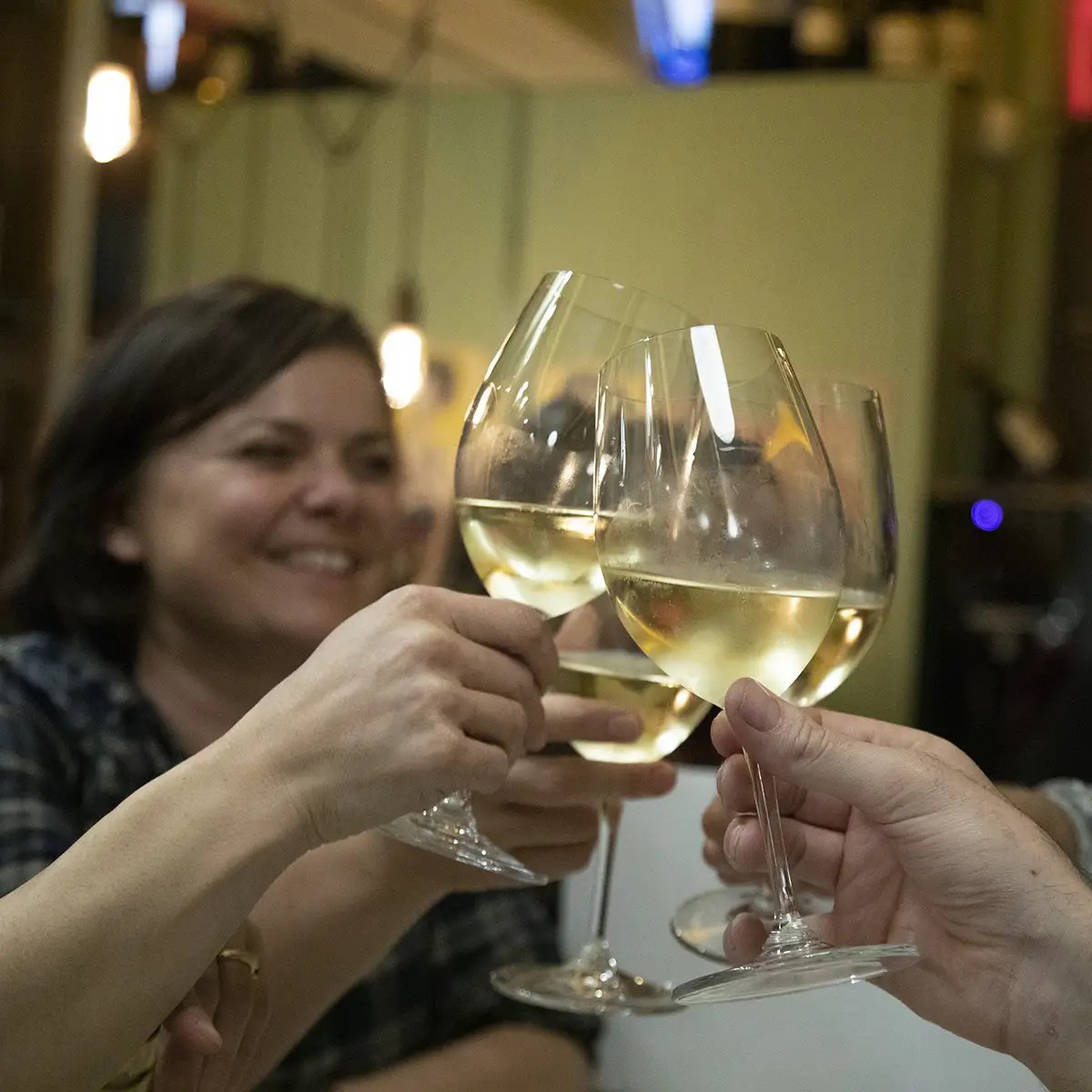 Three people toasting with white wine glasses at a social gathering.