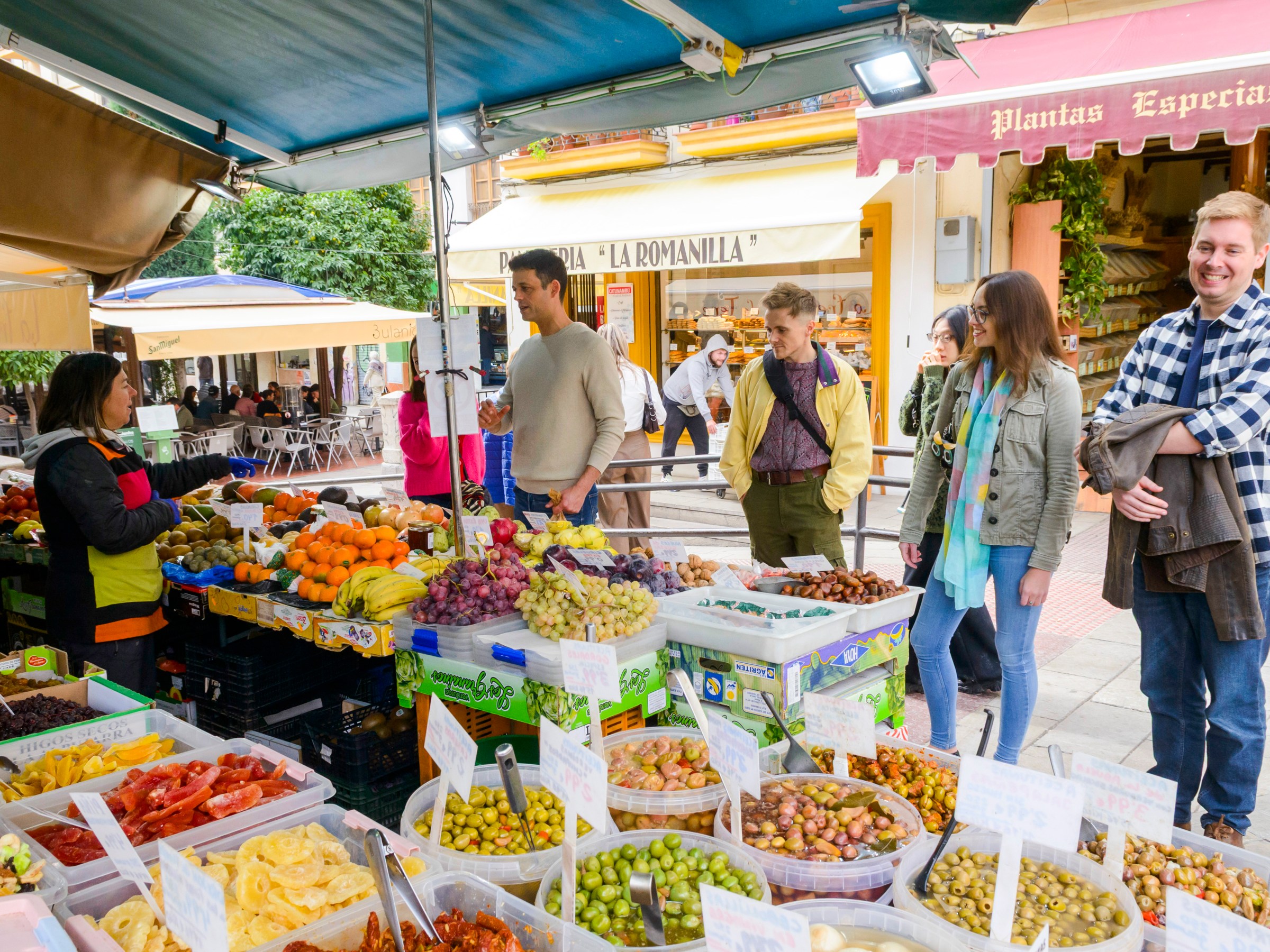 People browsing fruit and vegetable stalls at an outdoor market.