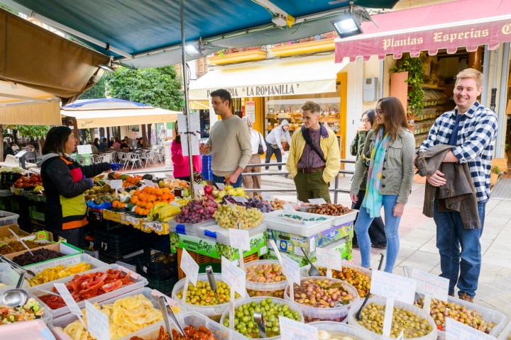 People browsing fruit and vegetable stalls at an outdoor market.