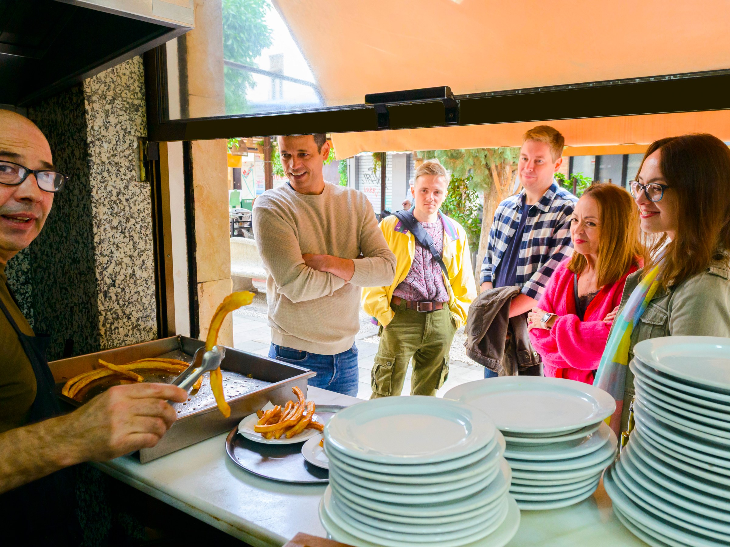 Cook serving churros to smiling people outside a café window.