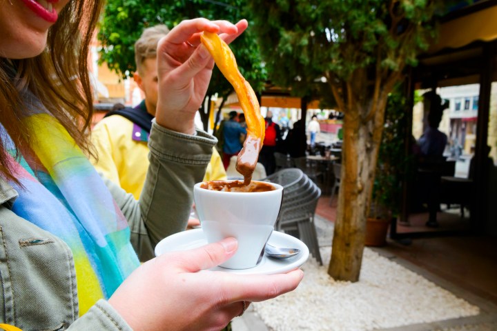 Person holding churro dipped in chocolate at an outdoor café.