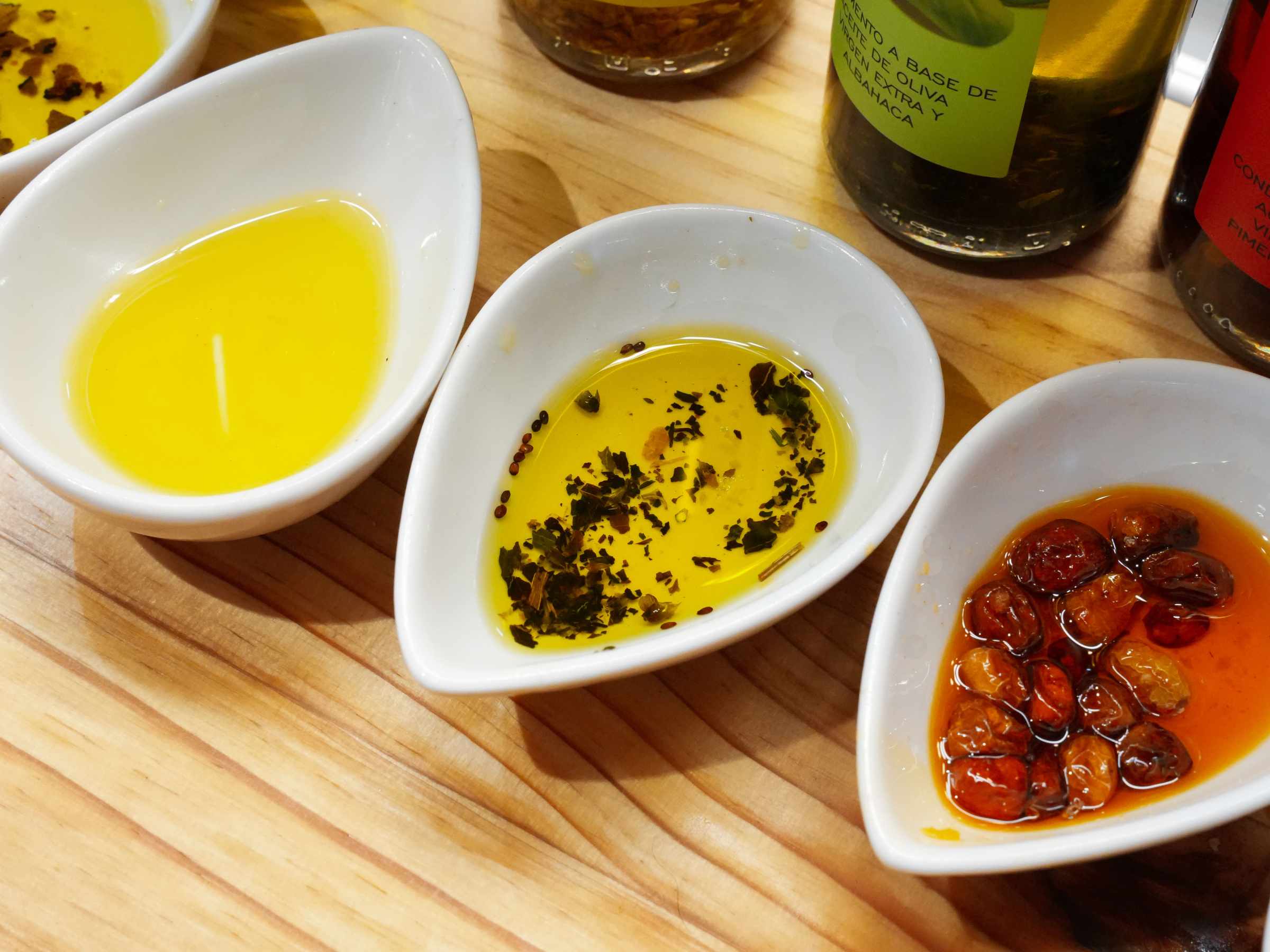 Three bowls with olive oil, seasoned oil, and oil with roasted garlic on a wooden table.