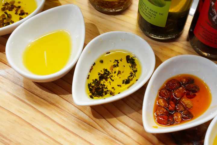 Three bowls with olive oil, seasoned oil, and oil with roasted garlic on a wooden table.