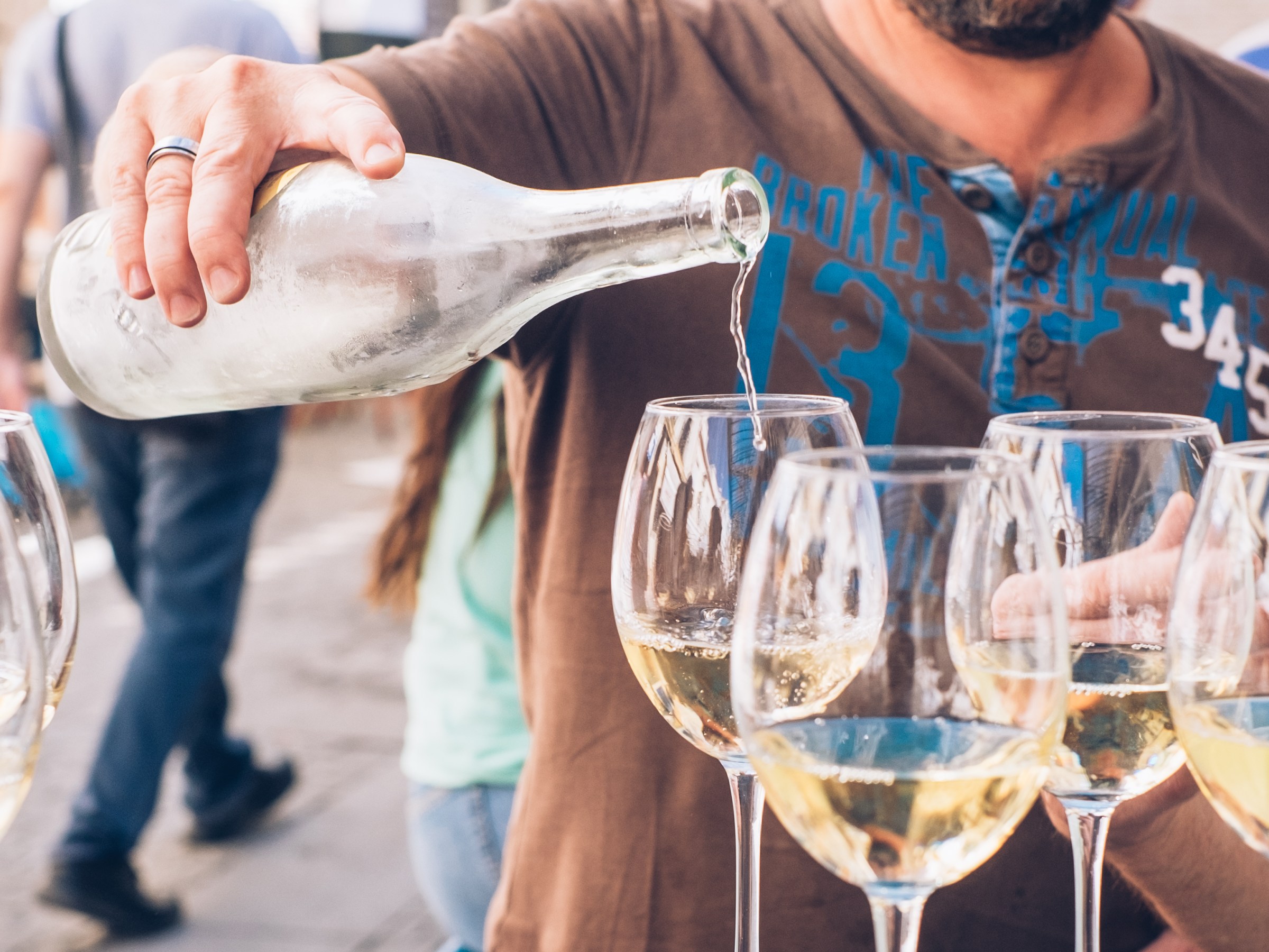 Person pouring wine into glasses at an outdoor event.