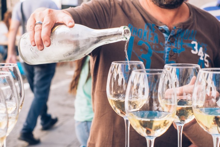 Person pouring wine into glasses at an outdoor event.