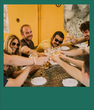 Group of people clinking glasses around a table, smiling and celebrating.