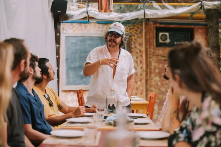 A man in sunglasses speaking to seated people at an outdoor gathering.