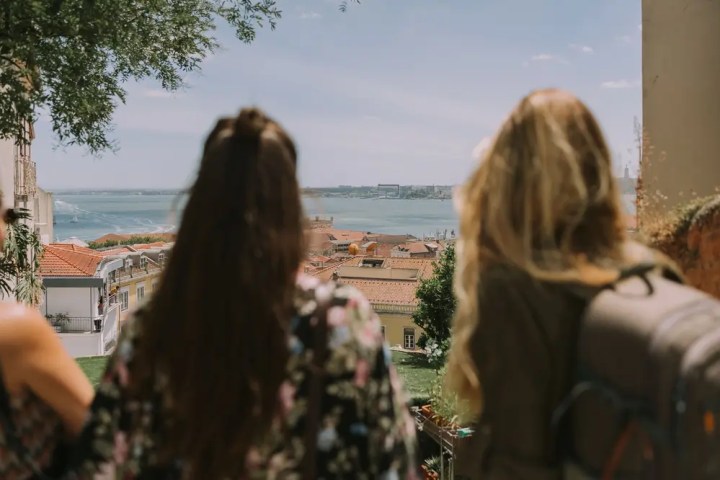 Two women with long hair overlook a scenic coastal city view.