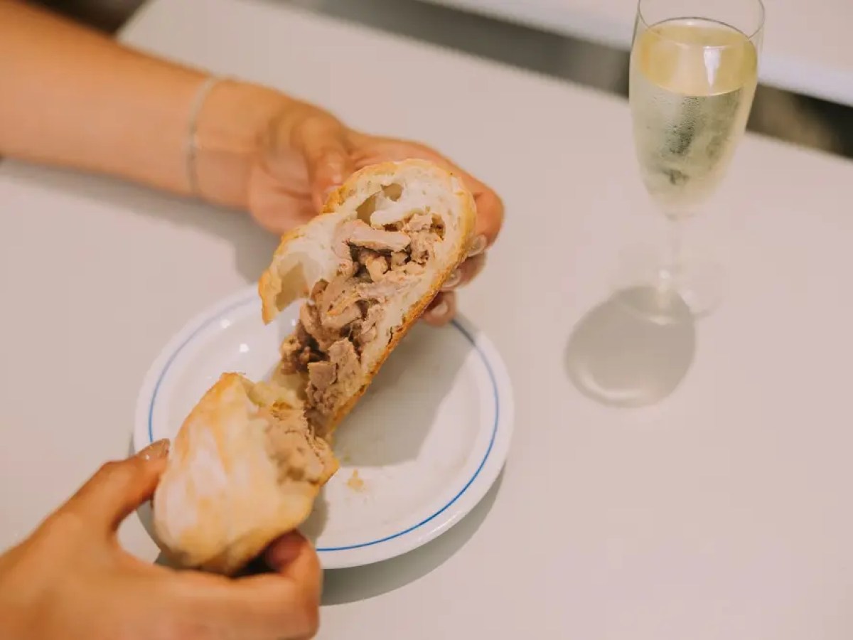 Person holding bread with meat filling over a plate beside a glass of champagne.