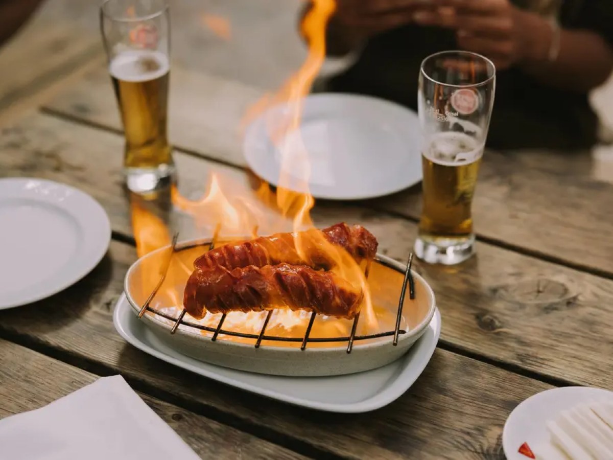 Grilled sausages on fire with two glasses of beer on a wooden table.