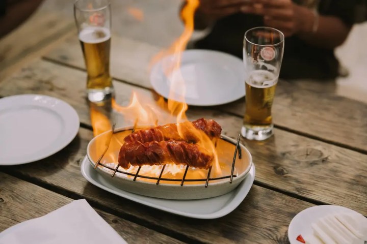 Grilled sausages on fire with two glasses of beer on a wooden table.