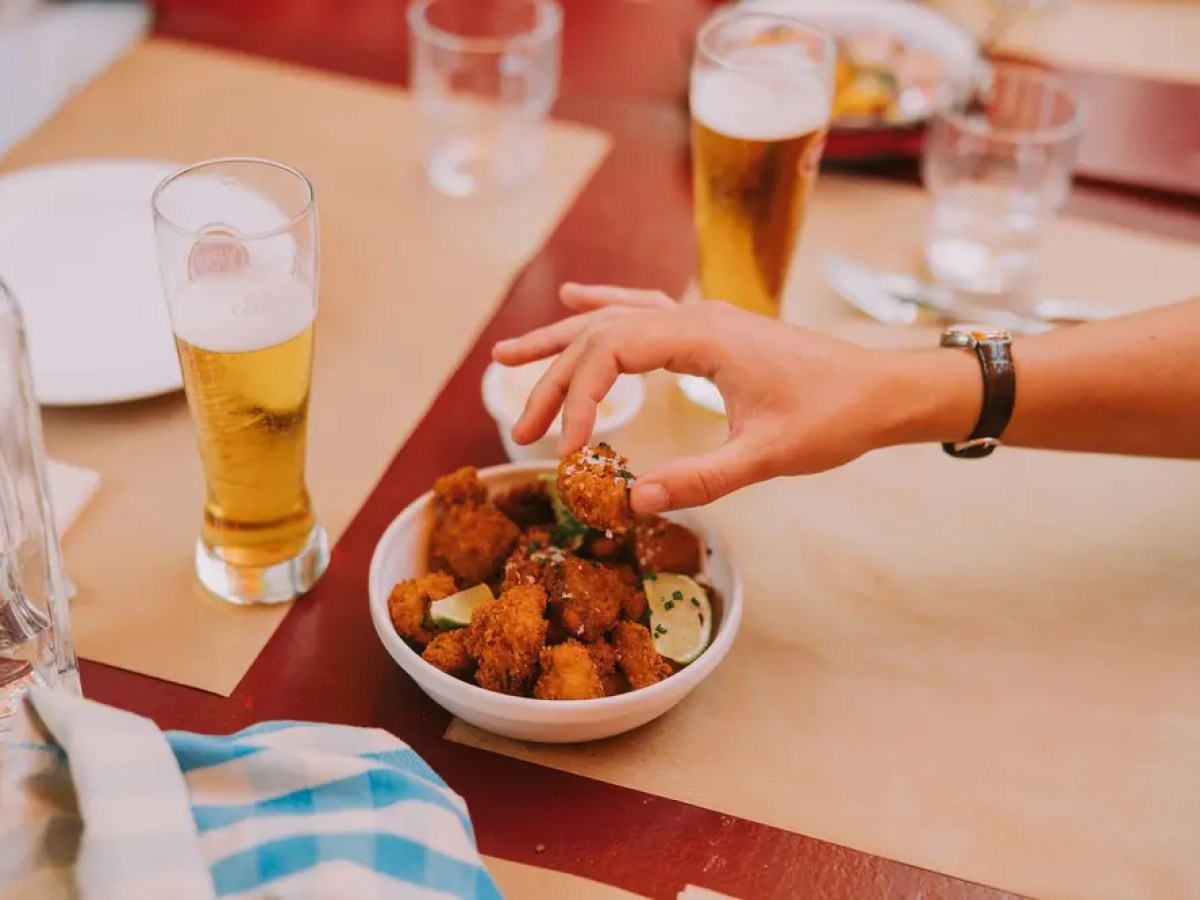 Person grabbing food from a bowl with drinks on a table.