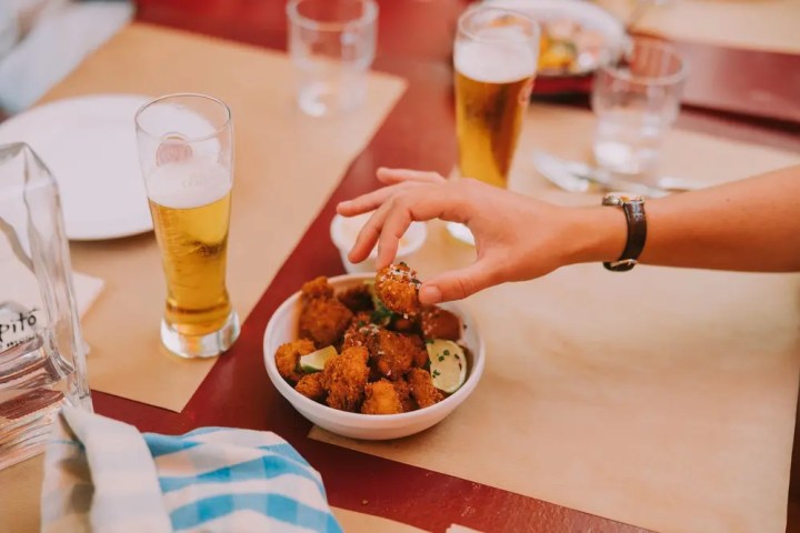 Person grabbing food from a bowl with drinks on a table.