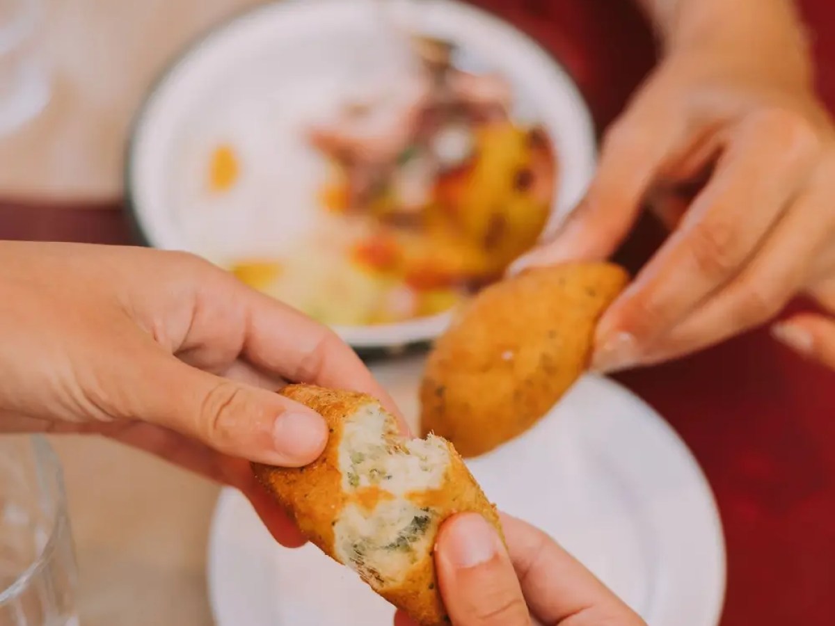 Hands breaking open a stuffed pastry over a plate on a table.