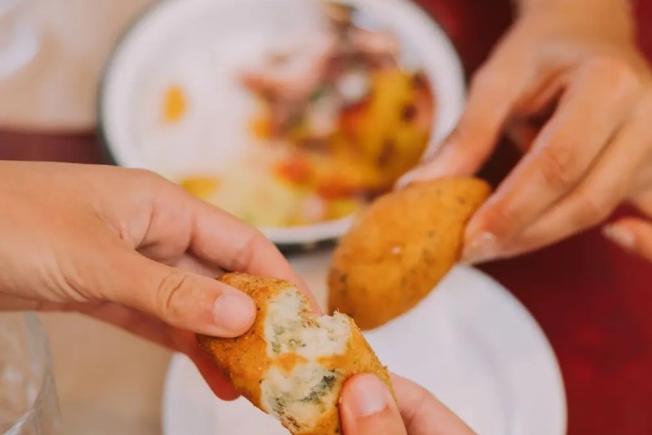 Hands breaking open a stuffed pastry over a plate on a table.